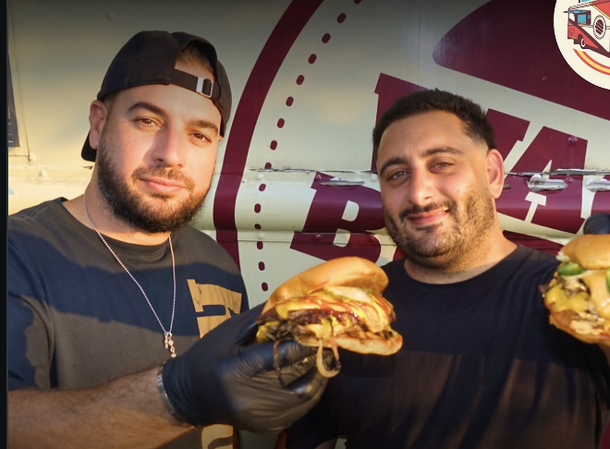 Alex and Harry holding Smosh Town burgers in front of the food truck